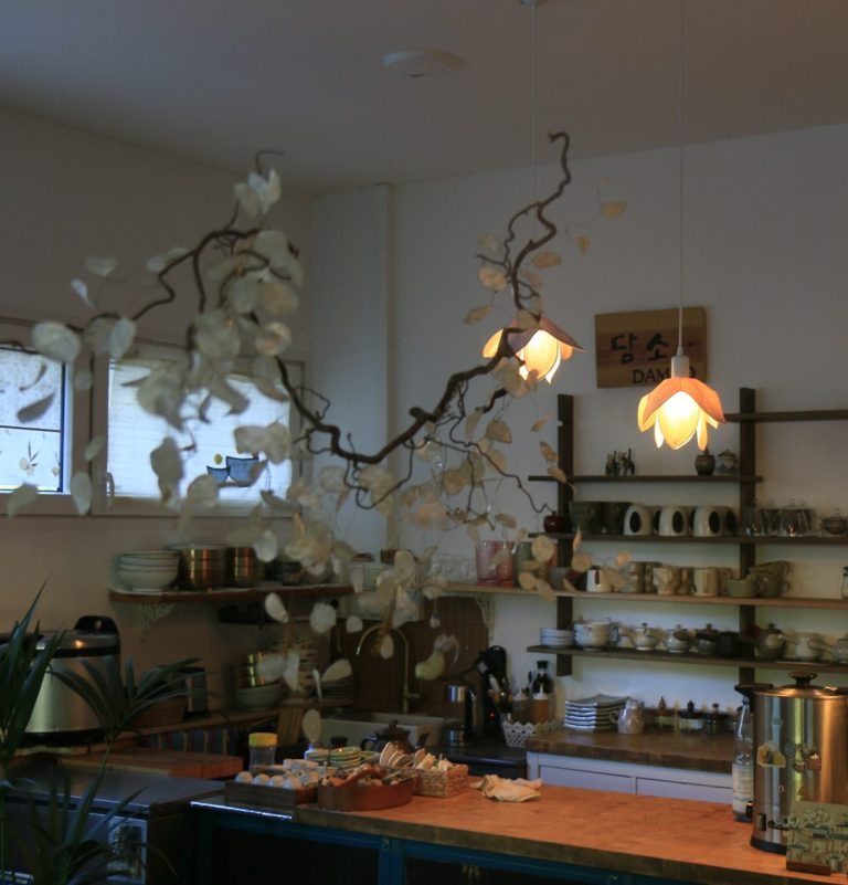 Holzschild mit der Aufschrift "DAMSO" über einem Regal mit Geschirr.